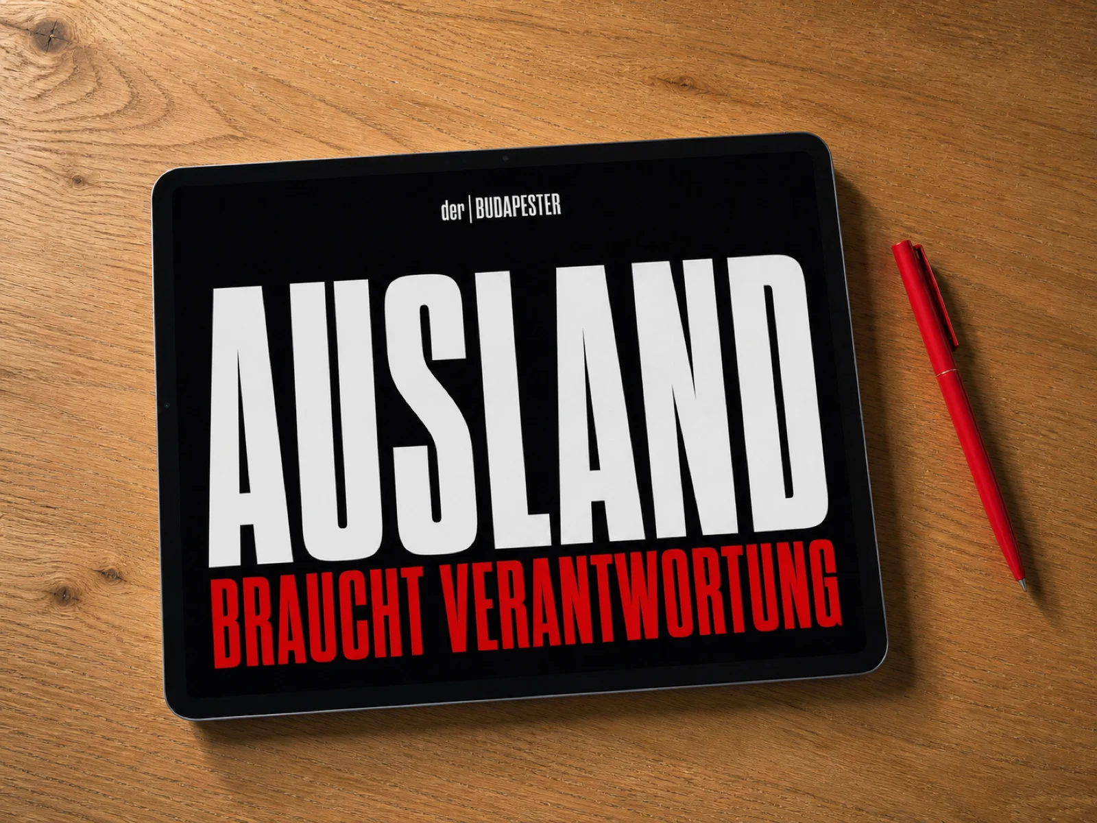 Schwarzes Tablet auf warmem Holztisch mit rotem Stift und lesbarem Text: Ausland braucht Verantwortung.